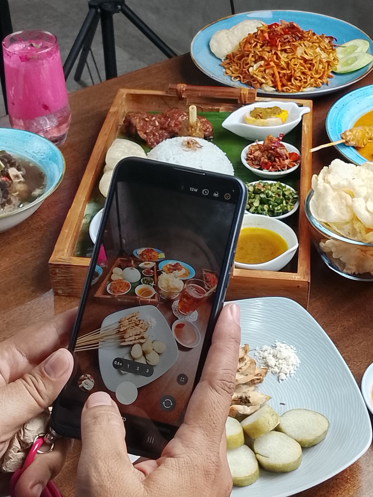 A smartphone photographing a table of Indonesian dishes.