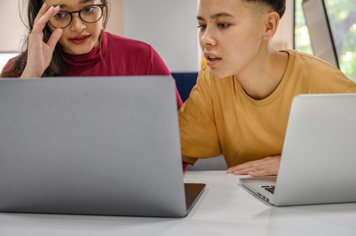 Two people discussing their work at a table with laptops.
